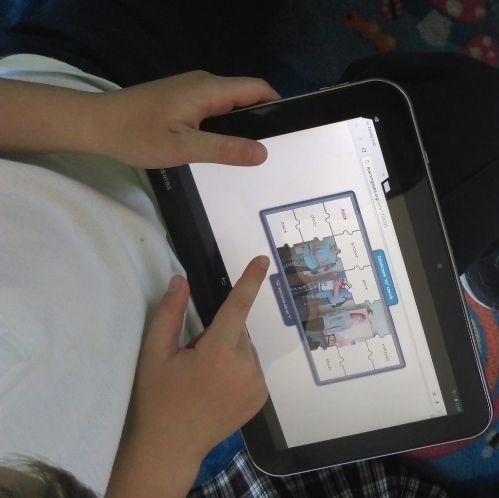 Dziecko trzyma tablet z otwartym ćwiczeniem interaktywnym w LearningApps